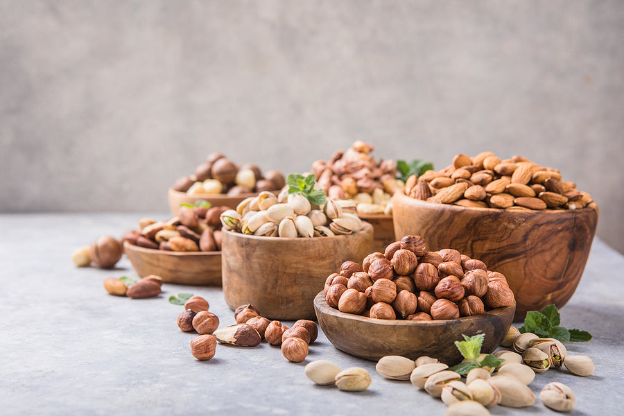 Assortment of nuts in a wooden bowls, on a gray background. Hazelnuts, pistachios, almonds, brazil nut, cashews. Nuts mix dried fruits in bowl, different kind of nut, healthy food on wooden table. Walnut, hazelnut, pistachio, peanut, almond. Assorted nuts