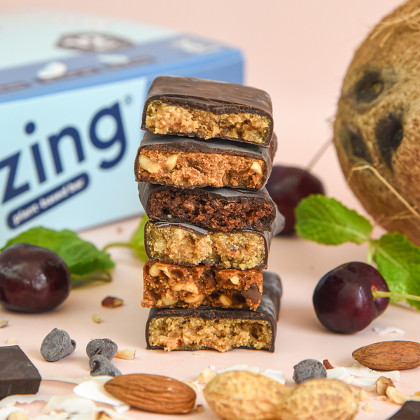 a variety of raw chocolate covered zing bars stacked surrounded by nuts and cherries