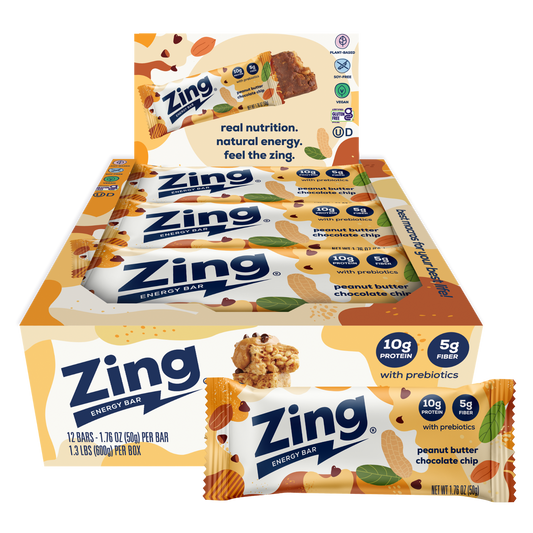 A display box and individual wrapped Zing Energy Bar snack bars on a plain white background. The packaging features orange, white, and blue colors with illustrations of almonds, chocolate pieces, and green leaves, and text indicating peanut butter chocolate chip flavor.